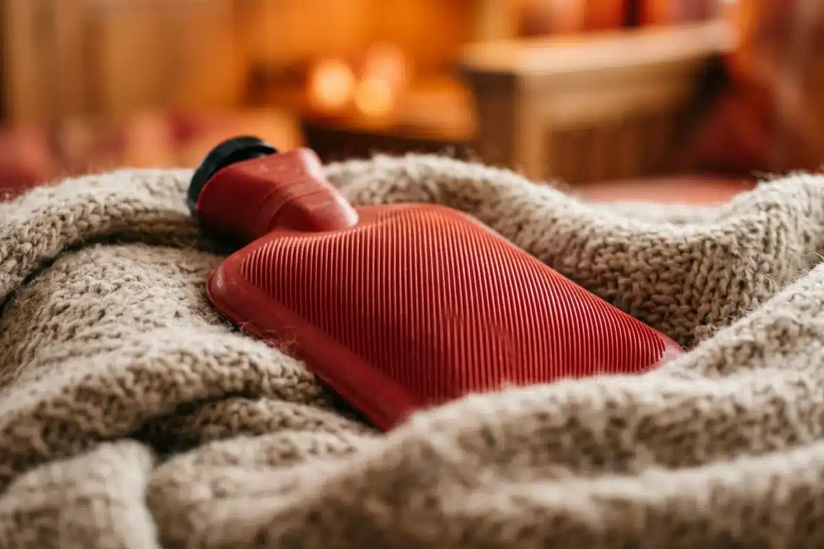 Bouillotte soulagement douleur ovulation Gros plan d'une bouillotte rouge posée sur un tissu de laine doux, atmosphère chaleureuse